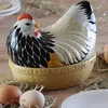 A ceramic chicken egg holder with a hen-shaped lid, placed on a bed of straw with real eggs around it. Náhled obrázku produktu