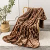 A brown patterned blanket draped over a wicker chair, with a plant in a basket to the left. Podgląd zdjęcia produktu