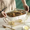 A person is holding a serving dish filled with food, which is placed on a warming stand with candles. Náhled obrázku produktu