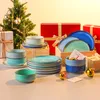 A collection of ceramic tableware, including plates and bowls, is arranged around a small, decorated Christmas tree and gift boxes. Produktbild-Vorschau