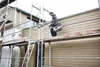 A construction worker is on scaffolding, working on the exterior of a building. Podgląd zdjęcia produktu