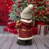 A Christmas-themed figurine of a child holding a teddy bear, standing in front of a decorated Christmas tree and wrapped gifts. Produktbild-Vorschau
