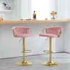 Two pink bar stools with gold legs and bases are shown in front of a bar with a white ribbed background. Produktbild-Vorschau