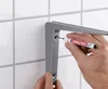 A person is using a marker to mark a hole on a shelf bracket mounted on a tiled wall. Produktbild-Vorschau