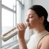 A woman drinks from a water bottle near a window. Produktbild-Vorschau