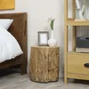 A bedside table with a tree stump design, placed next to a bed. A white vase with tulips and a picture frame are on top. Produktbild-Vorschau
