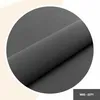 A close-up of a roll of dark gray fabric, displayed in a circular frame against a light cream and gray background. Anteprima dell’immagine prodotto