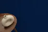 A beige toroidal vase sits on a round wooden table against a dark blue textured background. Produktbild-Vorschau