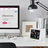 A desk setup with a computer monitor displaying an e-commerce page, a weather station, a desk lamp, and office supplies. Náhled obrázku produktu