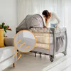 A woman is looking into a baby crib/playpen in a living room setting. There is a close-up inset showing airflow arrows. Produktbild-Vorschau