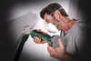 A man wearing safety gear is using a cordless rotary cutter to cut into a wall, with a vacuum hose attached to collect dust. Produktbild-Vorschau