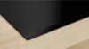 A close-up view of a black induction cooktop integrated into a light wood countertop. Voir les images du produit