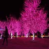 Trees decorated with pink lights at night, with people walking around. Produktbild-Vorschau
