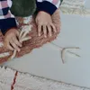 A child's hands are interacting with a textured rug with a chicken-like design. Voir les images du produit