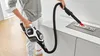 A person is using a cordless vacuum cleaner with a flexible hose attachment to clean a surface with small items on it. Voir les images du produit