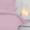 A pink duvet cover and pillowcase are neatly arranged on a bed, with two cylindrical lamps providing soft illumination in the background. Produktbild-Vorschau