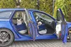 Two small dogs are sitting in blue car seats inside a blue car with the doors open. Produktbild-Vorschau