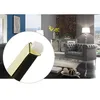 A close-up of a gold furniture leg with a white cap, superimposed on a lifestyle image of a modern living room with a gray tufted sofa and mirrored cabinet. Produktbild-Vorschau