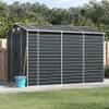 A dark gray metal shed is shown outdoors on a paved surface, with a wooden fence and trees in the background. A blue bucket and some garden tools are placed next to the shed. Podgląd zdjęcia produktu