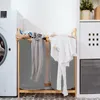 A laundry room scene with a washing machine, a bamboo laundry sorter with two gray bags, and clothes hanging to dry. Náhled obrázku produktu