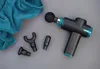 A massage gun and its attachments are laid out on a gray surface next to a teal towel. Produktbild-Vorschau