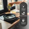 A person is pouring oil into a frying pan on an induction stove, with a protective mat underneath the pan. There is a bowl of food in the background. Anteprima dell’immagine prodotto