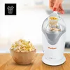 A popcorn machine is shown on a wooden table with a bowl of popcorn next to it. A hand is adding popcorn kernels to the machine. Anteprima dell’immagine prodotto