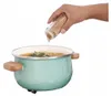 A hand is adding spices from a spice jar into a pot of soup. Náhled obrázku produktu