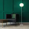 A modern living room scene with a black armchair, a round brown ottoman, and a floor lamp. Produktbild-Vorschau
