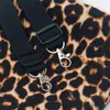 A close-up view of two black straps with silver clasps attached to a leopard-print fabric. Produktbild-Vorschau