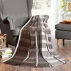 A striped blanket draped over a gray armchair next to a basket and books. Produktbild-Vorschau