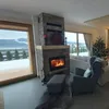 A cozy living room with a fireplace, Christmas tree, and large windows overlooking a snowy landscape. Produktbild-Vorschau