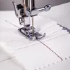 A close-up shot of a sewing machine needle and foot stitching a piece of white fabric with red thread. Produktbild-Vorschau