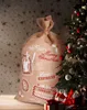 A large burlap sack with Christmas-themed designs is placed next to a decorated Christmas tree. Podgląd zdjęcia produktu