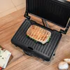 A panini grill with a sandwich on it, placed on a wooden table. Produktbild-Vorschau