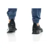 A close-up view of a person's feet wearing black Puma sneakers and blue pants, shown from the back and side. Produktbild-Vorschau