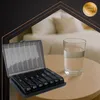 A pill organizer and a glass of water are placed on a wooden table in front of a blurred bedroom background. A golden seal with text is in the upper right corner. Náhled obrázku produktu
