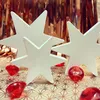 Three white wooden stars are arranged on a gold geometric patterned surface, with red gem-like objects scattered around them. A shimmering rose gold fringe hangs in the background. Produktbild-Vorschau