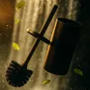 A toilet brush and holder are shown in a dynamic, almost floating composition with water droplets and leaves, set against a blurred waterfall-like background. Anteprima dell’immagine prodotto