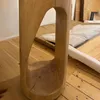 A close-up of a wooden table with a carved-out section, placed on a wooden floor with some packaging in the background. Produktbild-Vorschau