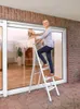 A woman is cleaning a large window while standing on a step ladder. Náhled obrázku produktu