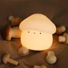 A glowing mushroom-shaped night light surrounded by wooden mushroom toys on a brown fabric surface. Podgląd zdjęcia produktu