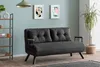 A dark gray sofa bed is shown in a living room setting with artwork on the wall and a plant. Náhled obrázku produktu