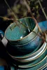 A stack of ceramic bowls and plates with a speckled green and blue glaze. Anteprima dell’immagine prodotto