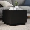 A black coffee table with two cups and a plant on it, placed in a living room setting with a sofa in the background. Produktbild-Vorschau