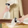 Two hands are shown using a portable garment steamer on a beige jacket and a piece of fabric. Produktbild-Vorschau