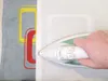 A hand is ironing a piece of fabric with a colorful design on it, next to a white piece of fabric. Anteprima dell’immagine prodotto