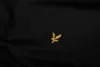 A close-up of a black t-shirt with a gold eagle logo. Produktbild-Vorschau