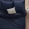 A close-up view of a bed with navy blue bedding and a decorative cream pillow. Podgląd zdjęcia produktu