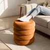A person's legs are resting on a stack of round, orange ottomans in a living room setting. Podgląd zdjęcia produktu